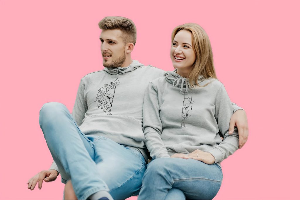 Couple wearing matching grey lion hoodies against a pink background