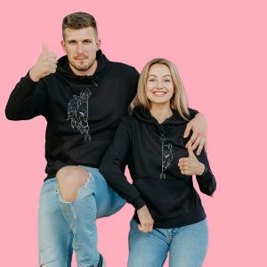 Couple wearing matching black lion hoodies, smiling and giving a thumbs up.