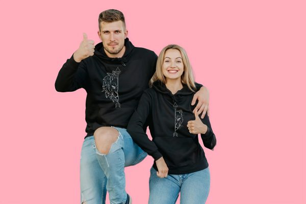 Couple wearing matching black lion hoodies, smiling and giving a thumbs up.